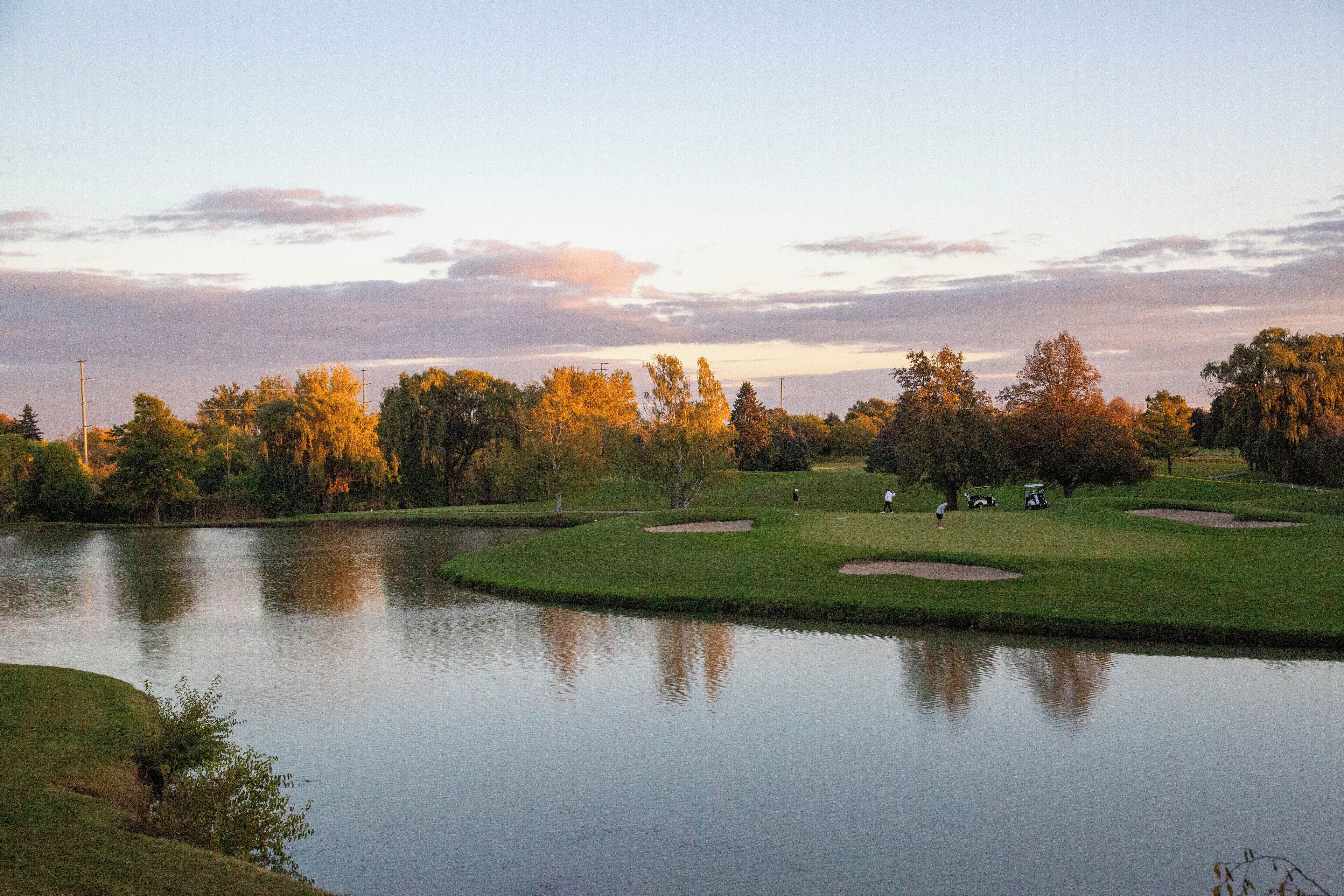 Un parcours de golf avec un étang, des arbres et un ciel dégagé.