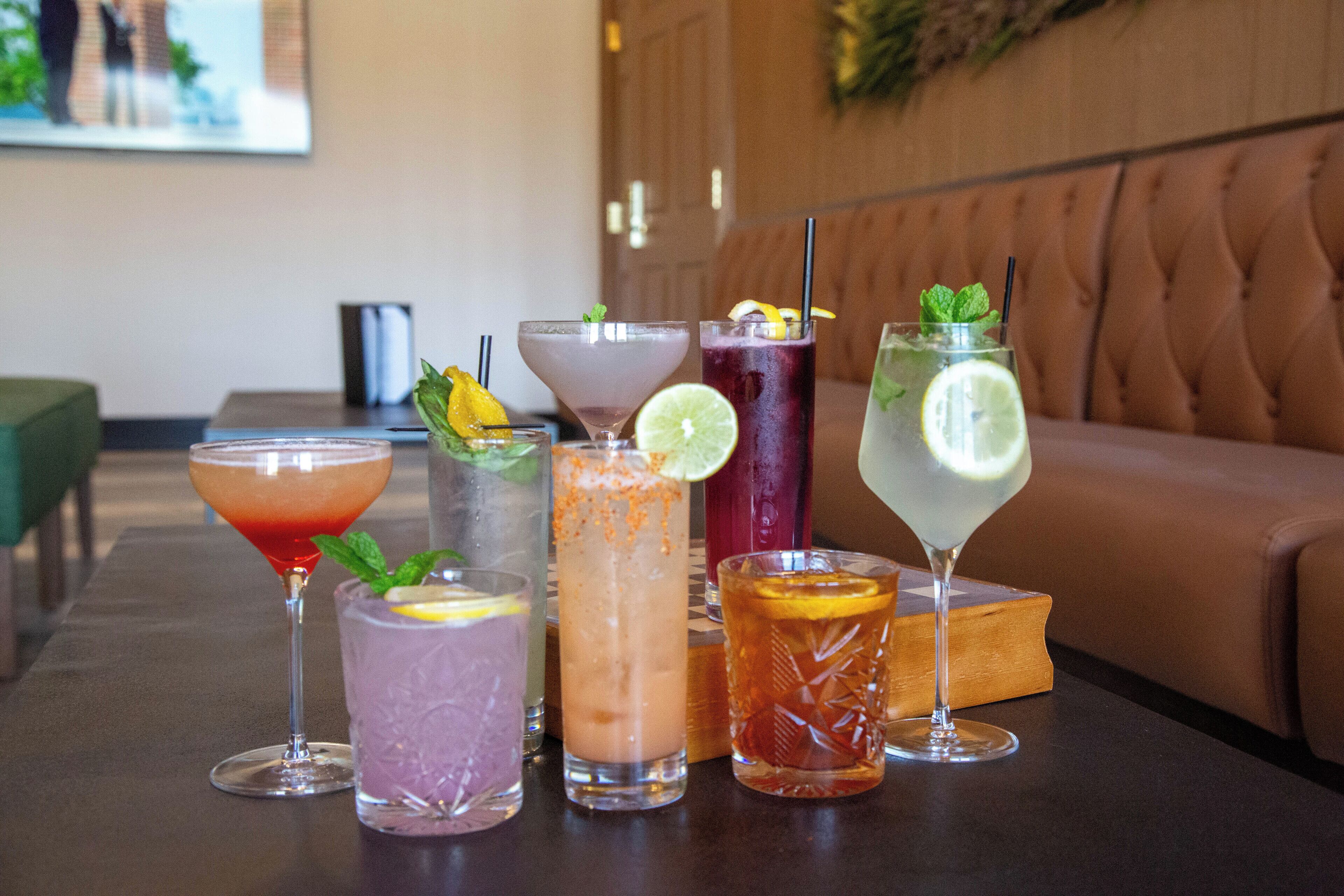 A table with various cocktails, a green couch, and a wooden book in the background.