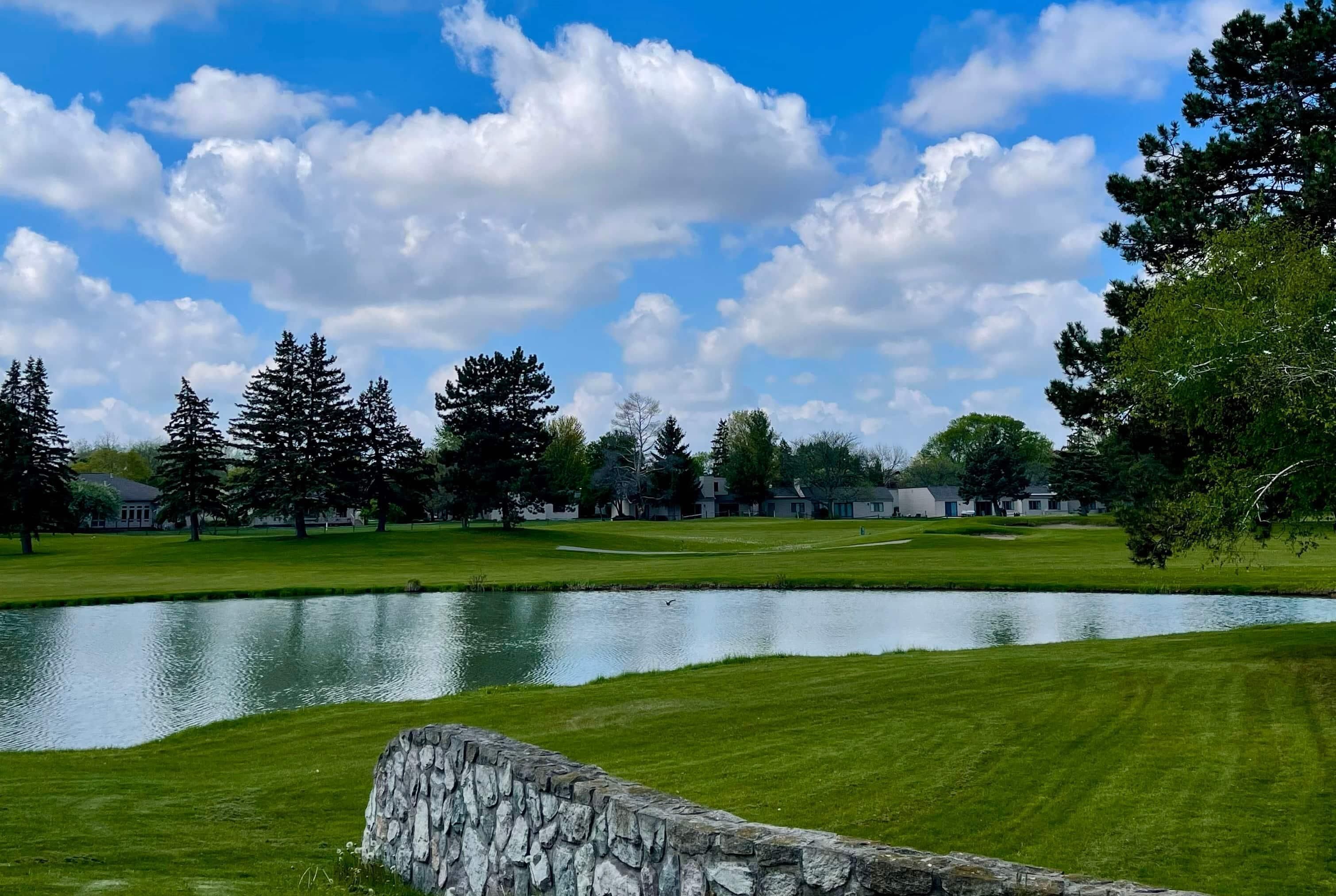 Un campo de golf con un estanque, un muro de piedra y árboles.