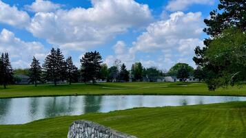 Un campo de golf con un estanque, un muro de piedra y árboles.