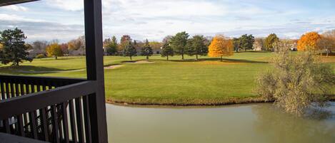 A view from a covered deck overlooking a grassy area with a pond and trees in autumn colors.