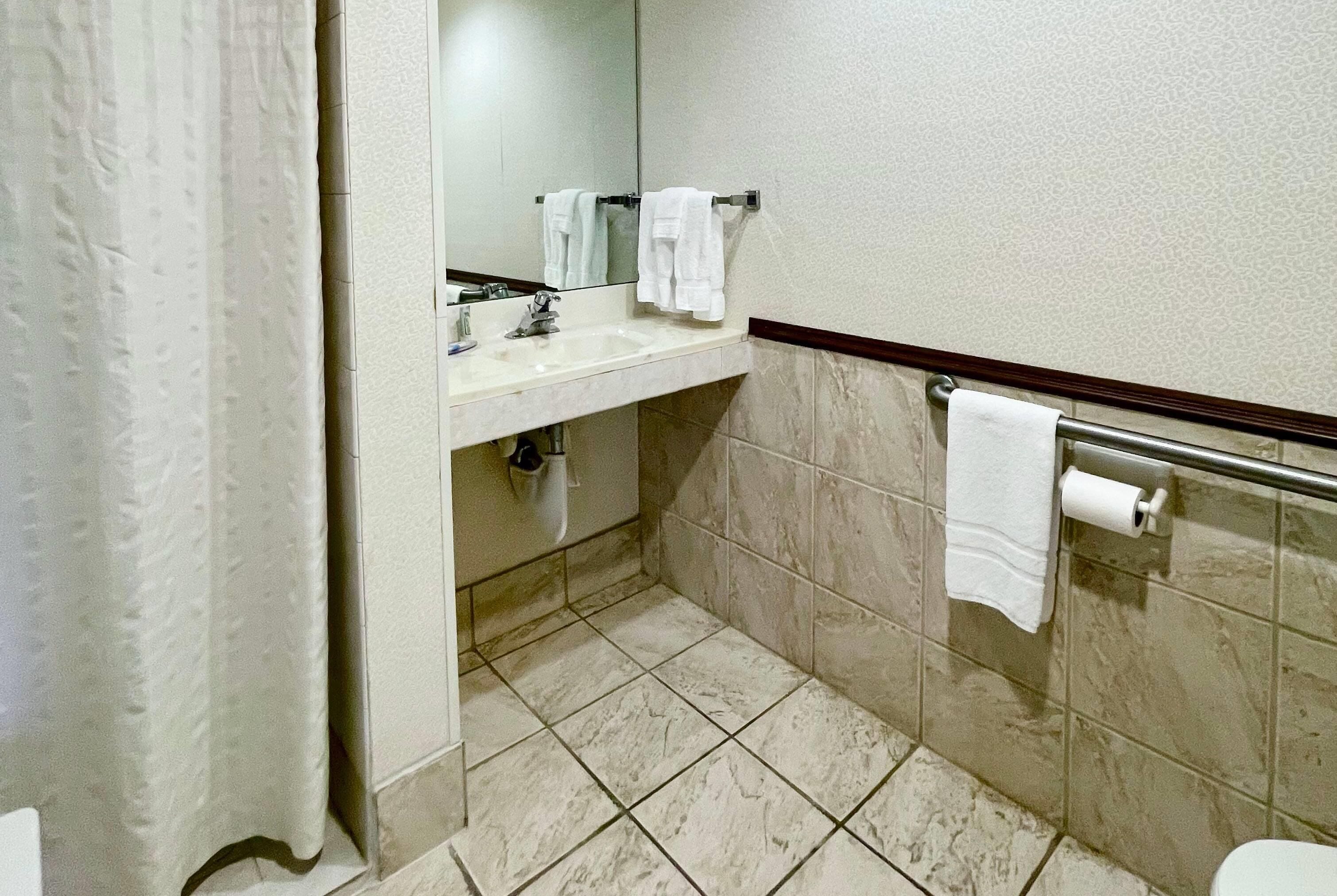 Un baño con lavamanos, espejo y dos toallas colgadas en la pared.
