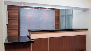 A reception area with a wooden panel wall, a glass partition, and a black reception desk. - Fairfield Inn & Suites Terre Haute (Terre Haute)