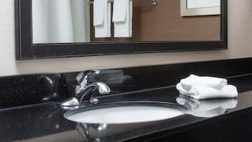A bathroom with a black countertop, a white sink, and a mirror reflecting a towel rack with white towels.