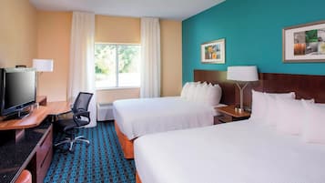 Een hotelkamer met twee bedden, een bureau met een televisie, een stoel en een raam met gordijnen.