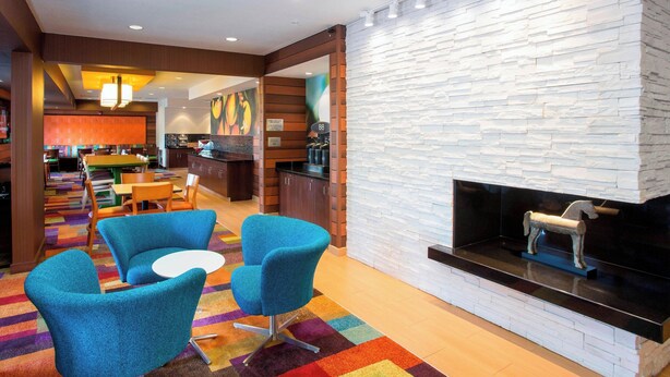 A modern hotel lobby with a stone wall fireplace, blue armchairs, a small table, and a colorful carpet. - Fairfield Inn & Suites Terre Haute (Terre Haute)