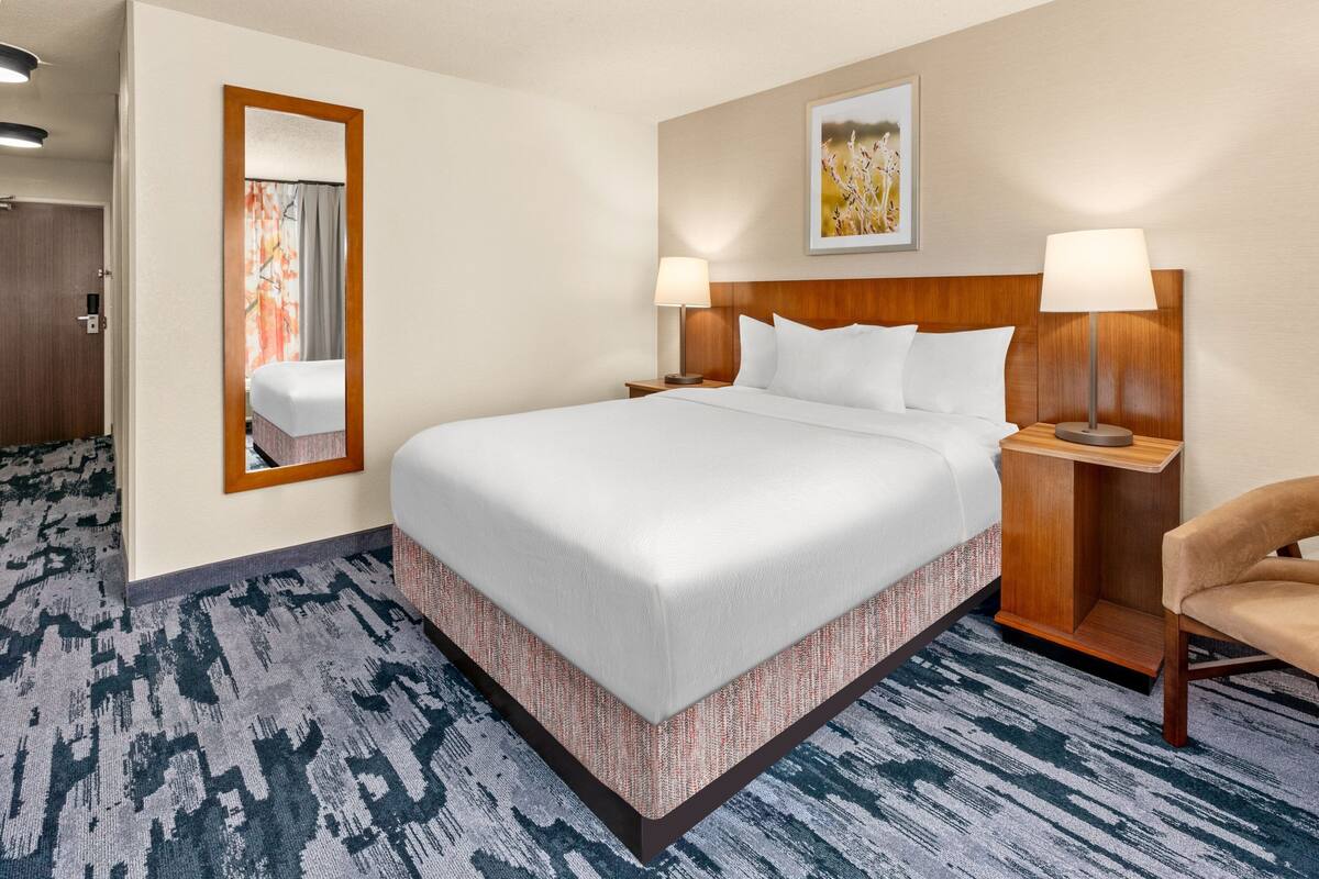 A hotel room with a large bed, two bedside tables with lamps, a mirror, and a carpeted floor.