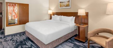 A hotel room with a large bed, two bedside lamps, a wooden headboard, a chair, and a painting on the wall.