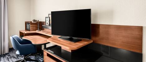 A hotel room with a wooden desk, a flat-screen TV, a blue office chair, and a small wooden cabinet.