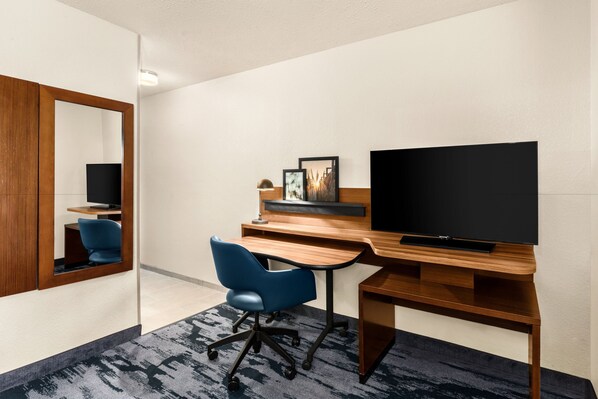 Una habitación de hotel con un escritorio de madera, una silla de oficina azul, un televisor y un espejo.