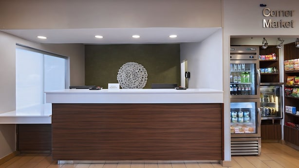 A reception area with a wooden counter, a decorative wall piece, and a refrigerator stocked with beverages.
