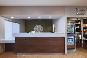 A reception area with a wooden counter, a decorative wall piece, and a refrigerator stocked with beverages.