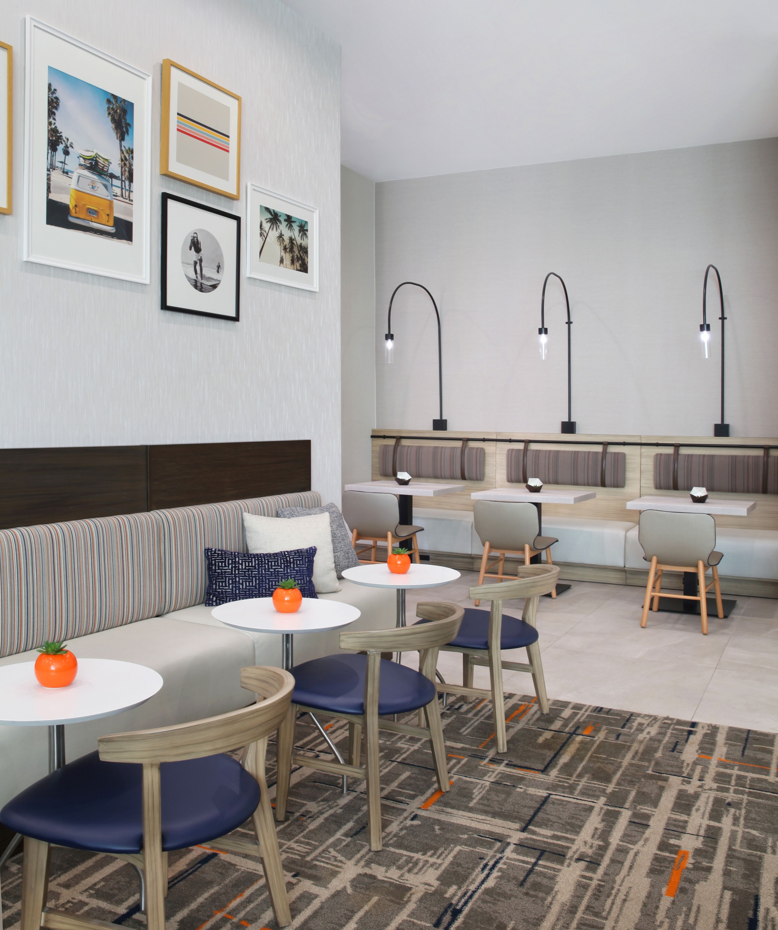 Une chambre d’hôtel moderne avec un canapé, des tables rondes et des chaises, un tapis à motifs et des œuvres d’art accrochées au mur.