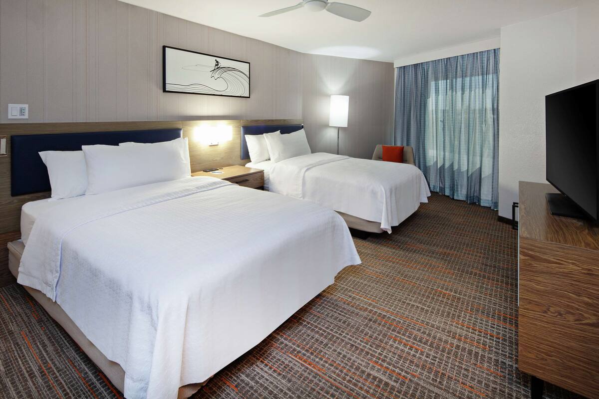 Une chambre d’hôtel avec deux lits, un ventilateur de plafond, un téléviseur à écran plat et une grande fenêtre avec des rideaux.