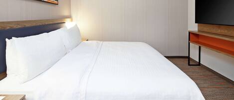 Une chambre d’hôtel dotée d’un grand lit, d’un téléviseur à écran plat, d’une tête de lit en bois et d’une œuvre d’art accrochée au mur.