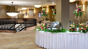 A hotel lobby with a grand staircase, a buffet table with floral centerpieces, and elegant lighting fixtures.
