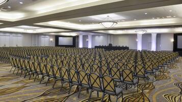 A conference room with rows of chairs, a stage, and a carpeted floor.