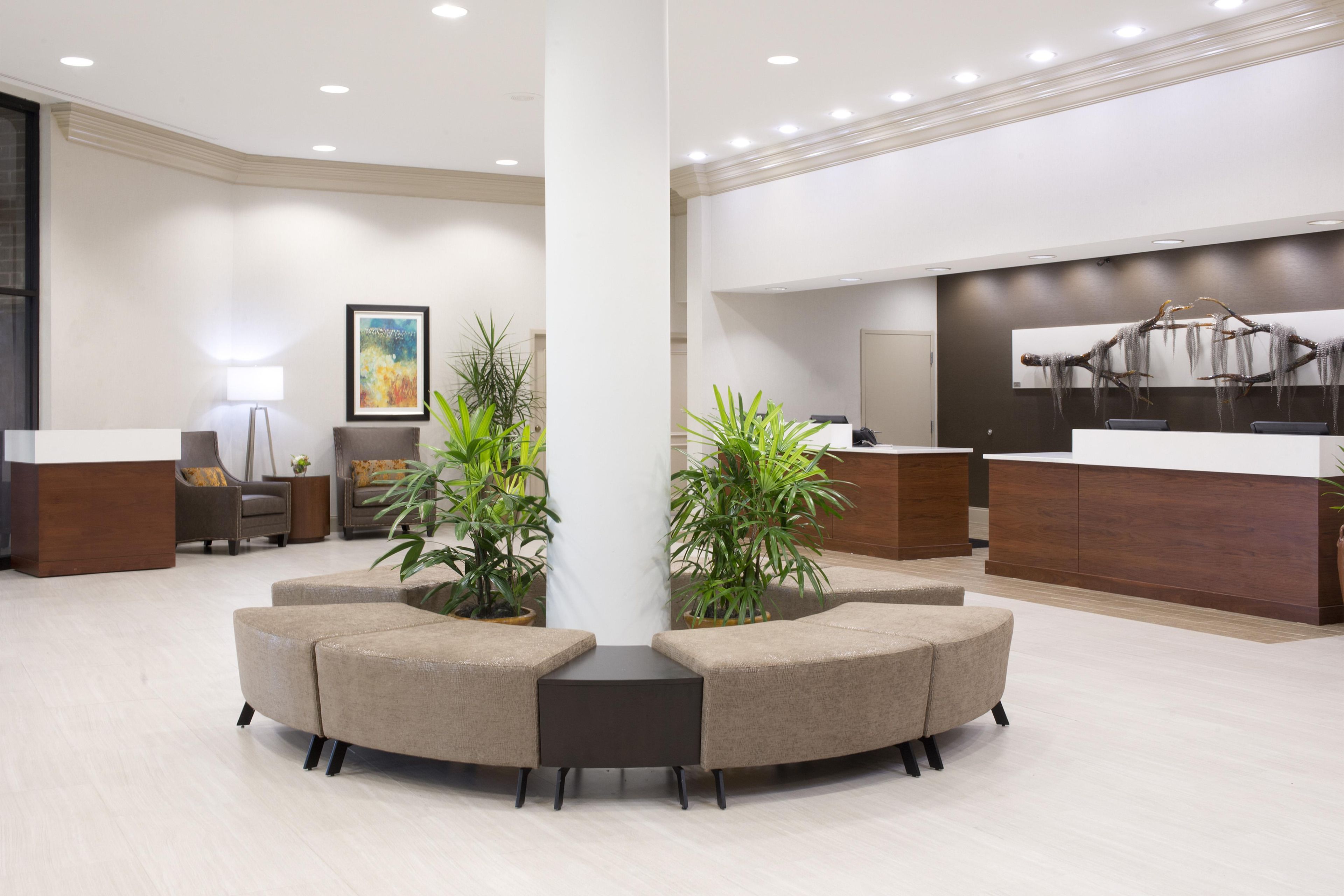 Una zona de recepción moderna con un arreglo de asientos central, un mostrador de recepción y un elemento decorativo en la pared.