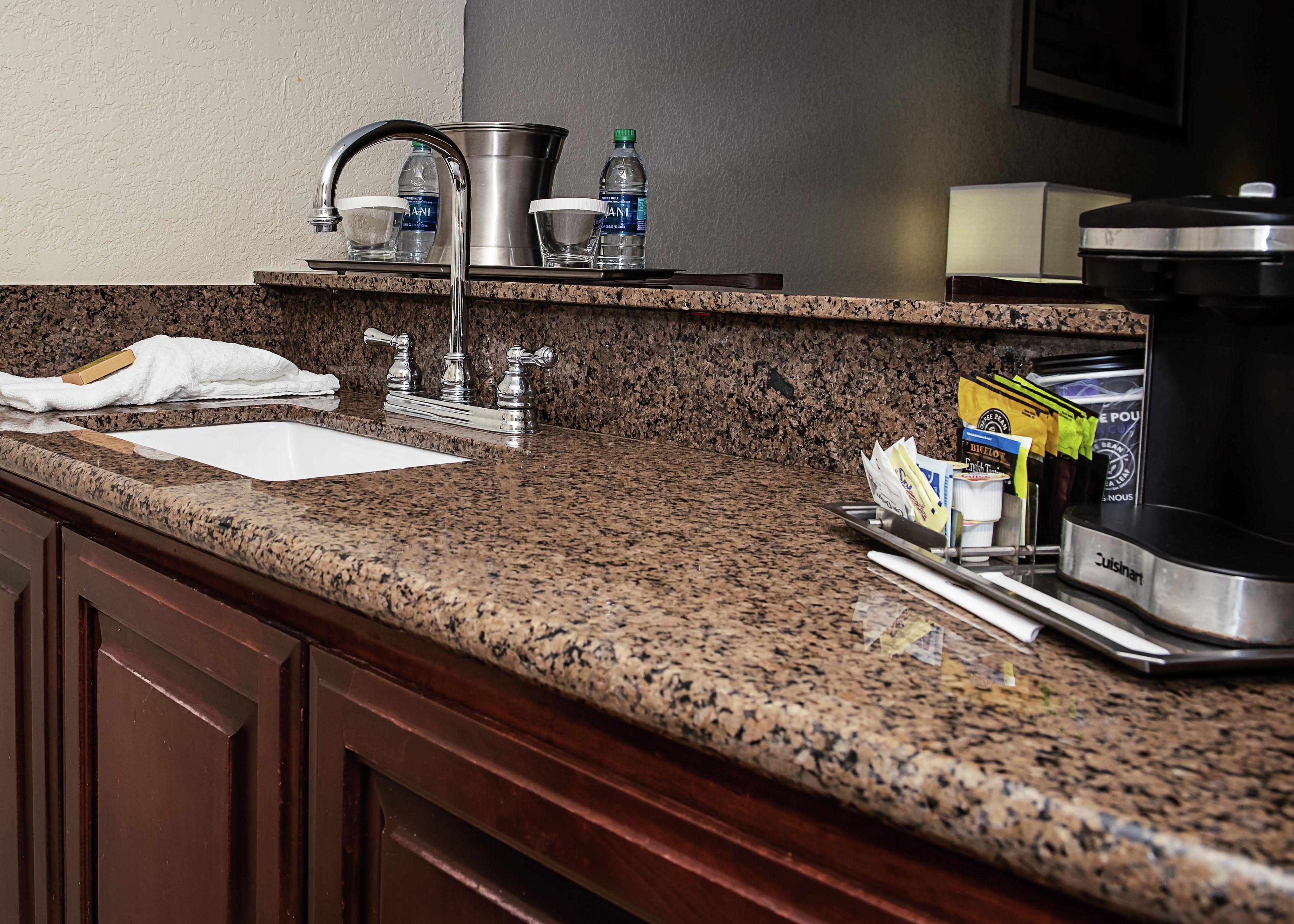 A kitchen with granite countertops, a stainless steel sink, a coffee maker, and a kettle.