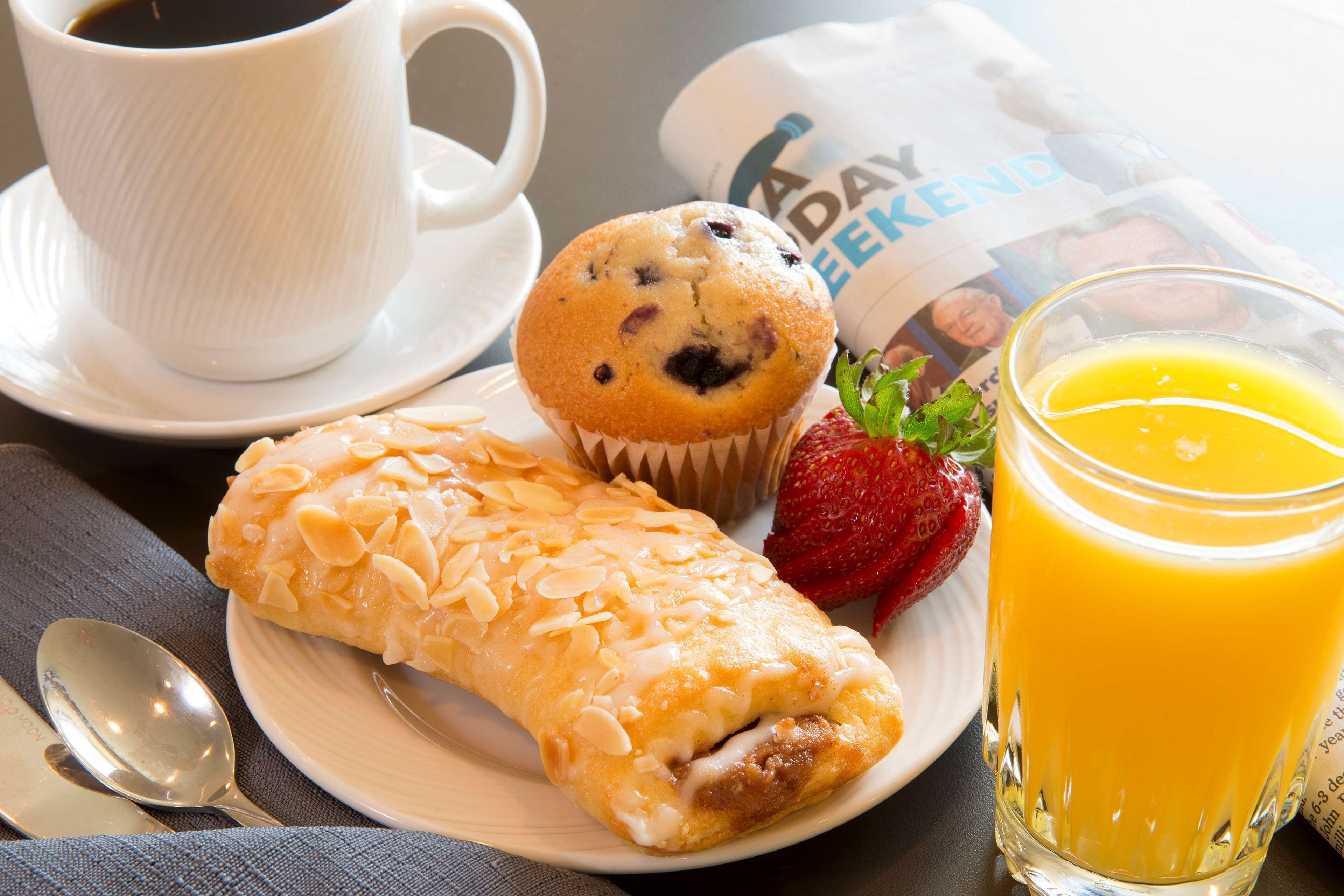 A breakfast plate with a muffin, a pastry, a strawberry, and a glass of orange juice.