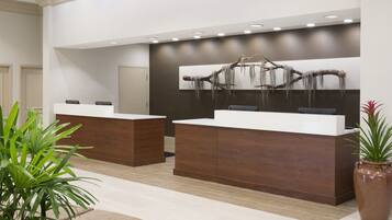A reception area with two reception desks, a large wall-mounted art piece, and a potted plant.