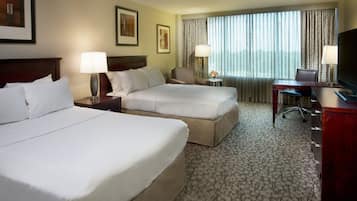 A hotel room with two beds, a desk, a TV, and a window with curtains.