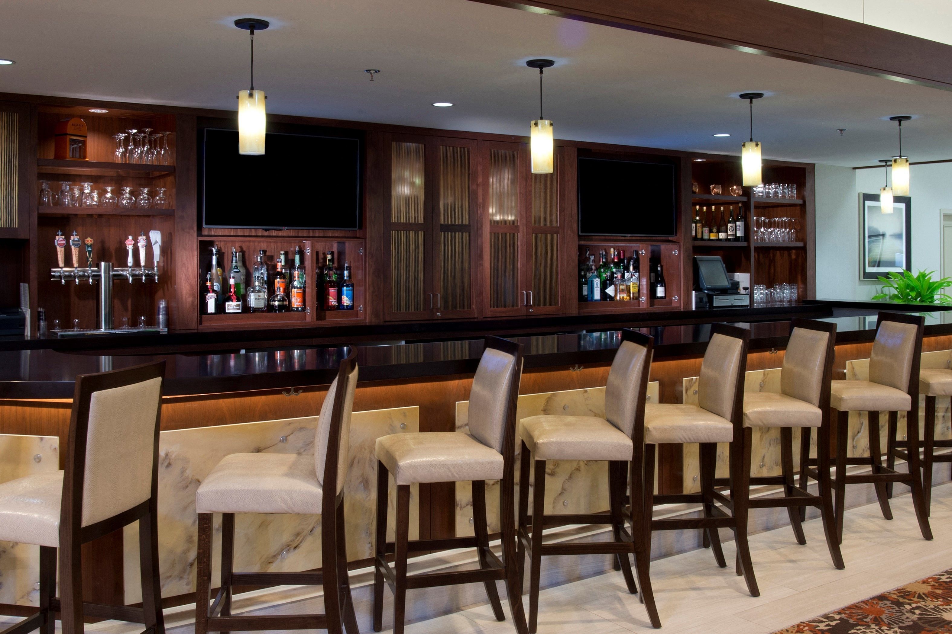 A bar area with multiple stools and a bar counter stocked with bottles and glasses.