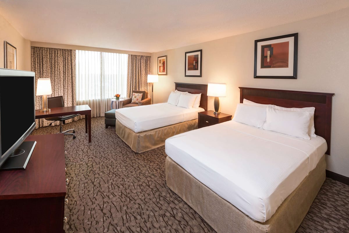 A hotel room with two beds, a desk, a TV, and a window with curtains.
