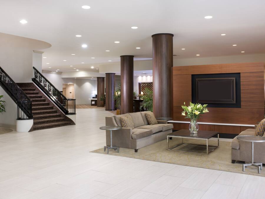 A spacious lobby with a staircase, a sofa, a coffee table, and a large wall-mounted TV.