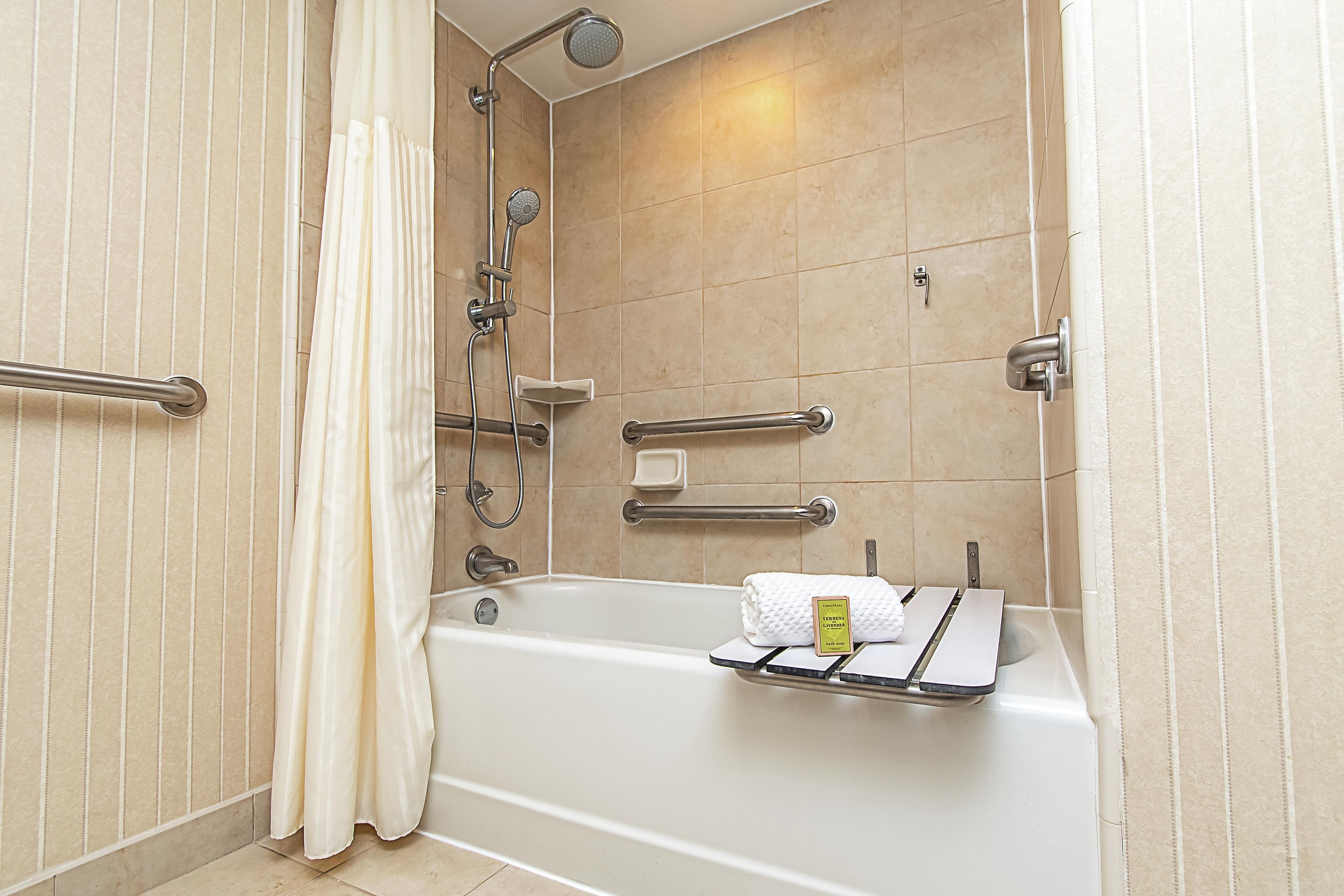 Een badkamer met een badkuip, douche, handgrepen en een handdoekrek.