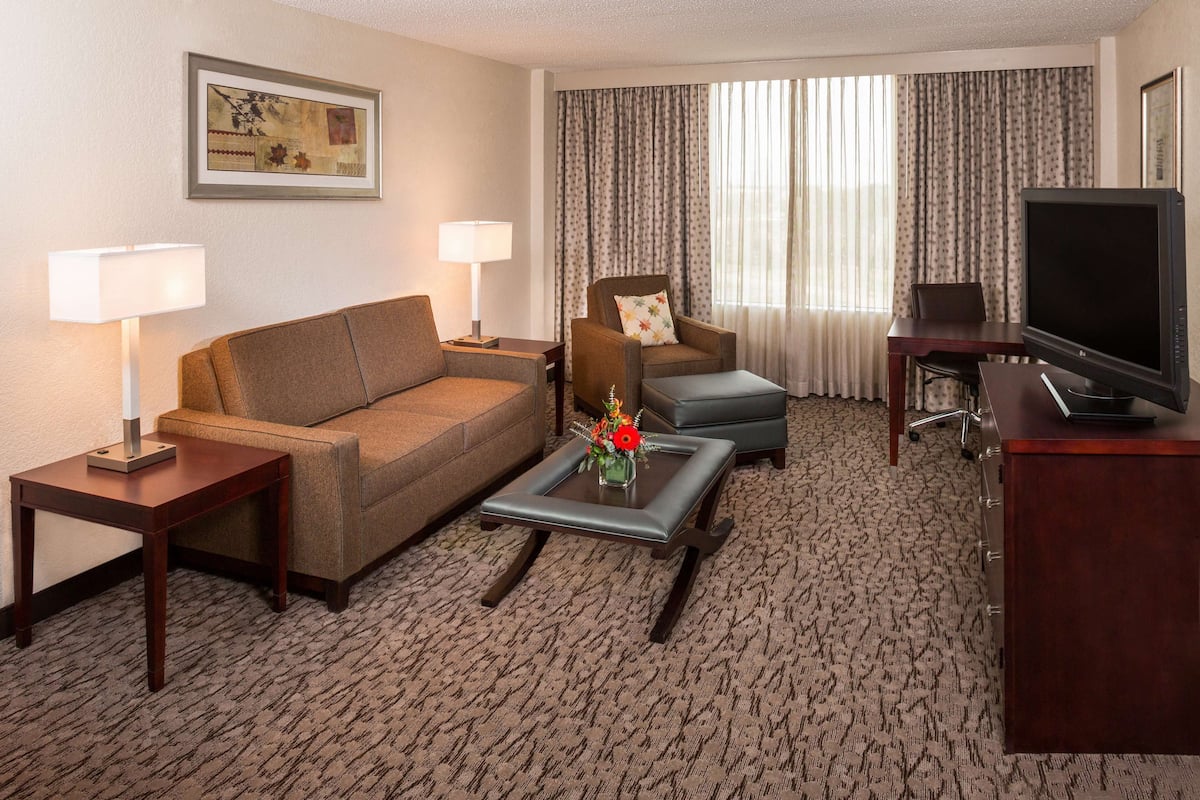A hotel room with a sofa, armchair, coffee table, TV, and a desk.