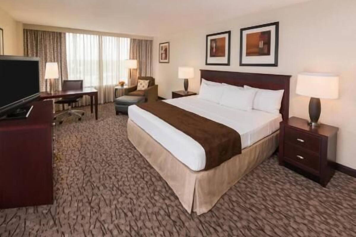 A hotel room with a large bed, a desk, a television, and two framed pictures on the wall.