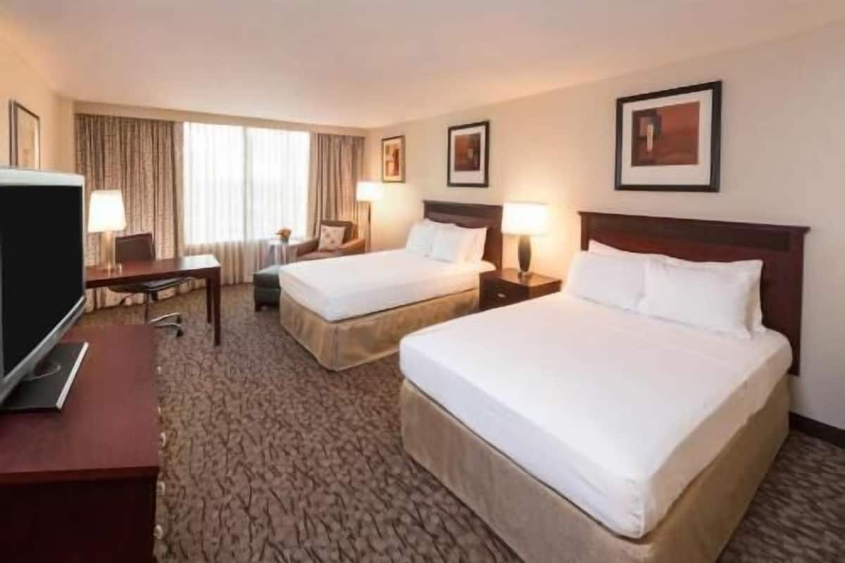 A hotel room with two beds, a desk, a TV, and a window with curtains.
