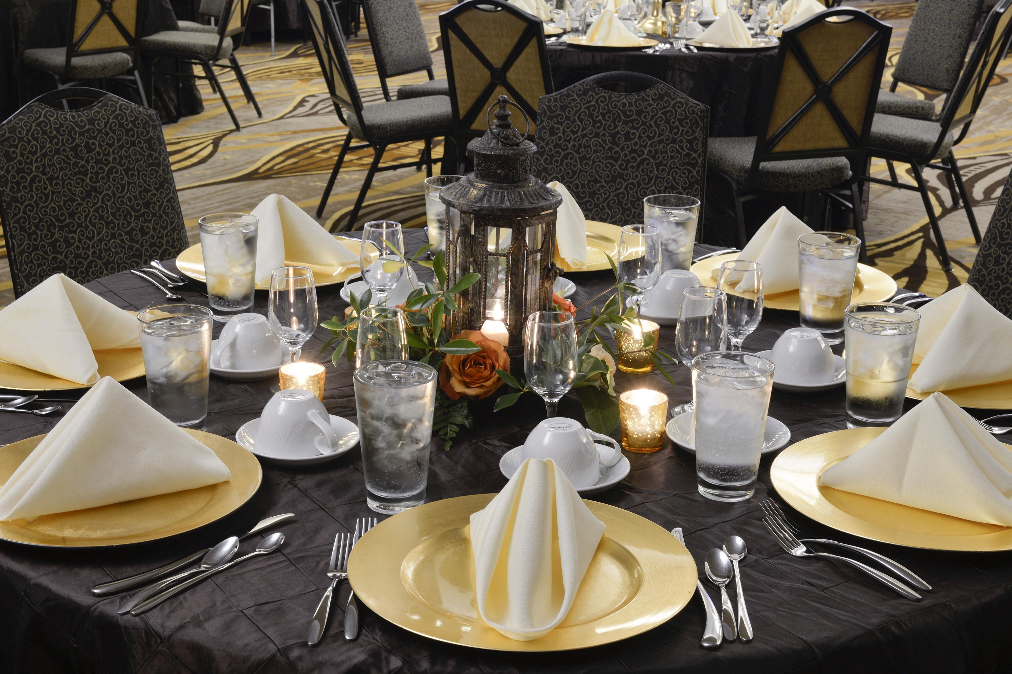 A table set for a formal dining event with gold and white tableware, clear glasses, and decorative candles.