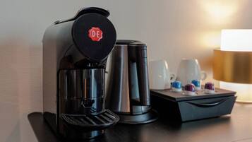 A coffee maker with a DE logo, a silver electric kettle, and a tray with cups and a teapot on a table.