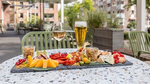 An outdoor dining table with a variety of cheeses, meats, and fruits, accompanied by a glass of beer and a wine glass. - Leonardo Hotel Breda City Center (Breda)