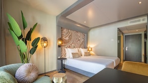 A modern hotel room with a bed, a sofa, a coffee table, and a large plant. - Leonardo Hotel Breda City Center (Breda)