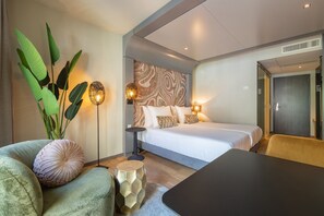 A modern hotel room with a bed, a sofa, a coffee table, and a large plant. - Leonardo Hotel Breda City Center (Breda)