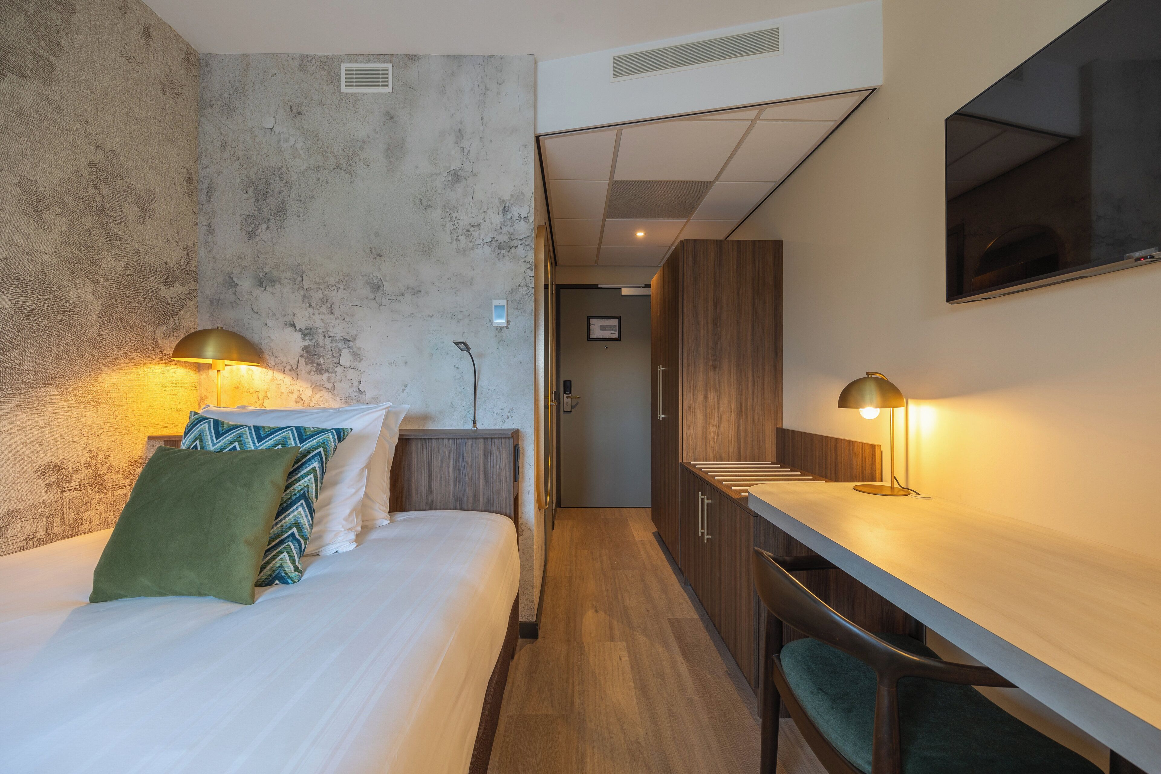 A modern hotel room with a bed, bedside lamps, a desk, and a mirror.