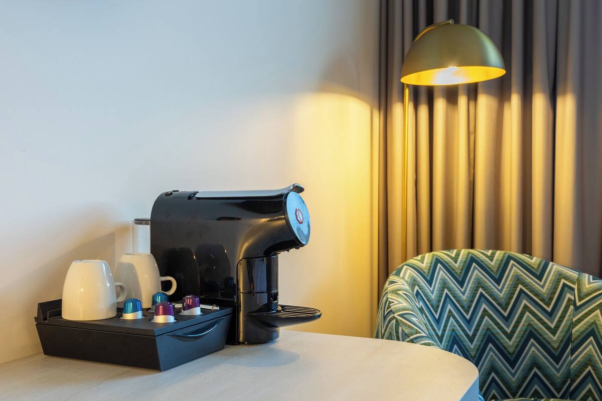 A coffee maker with a tray of cups and a lamp on a table.