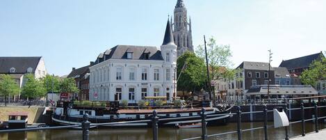 A historic building with a prominent tower, a canal with a boat, and a pedestrian walkway.