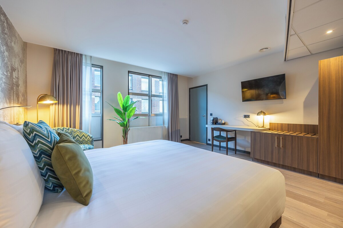 A modern hotel room with a large bed, a desk, and a TV.