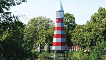 Een torenlamp met een kegelvormige constructie in een rood-wit gestreept patroon, gebouwd op palen boven water, omringd door weelderige begroeiing en bomen.