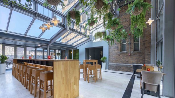 A modern interior with a long wooden bar, seating area, and hanging plants. - Leonardo Hotel Breda City Center (Breda)