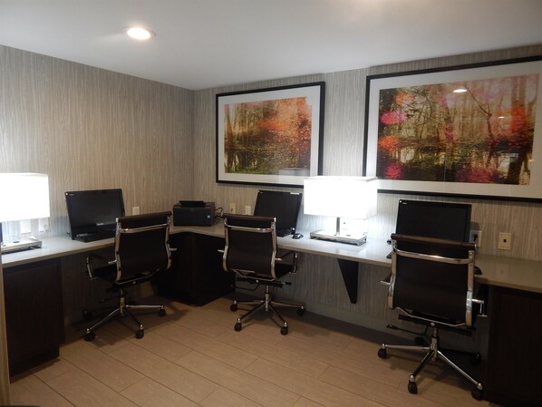 A conference room with four desks, each with a laptop and a printer, and two standing desks with chairs.