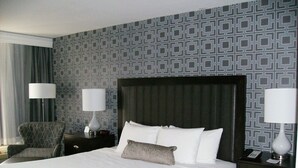 Une chambre d’hôtel avec un grand lit, deux tables de chevet, une chaise et un papier peint à motifs.