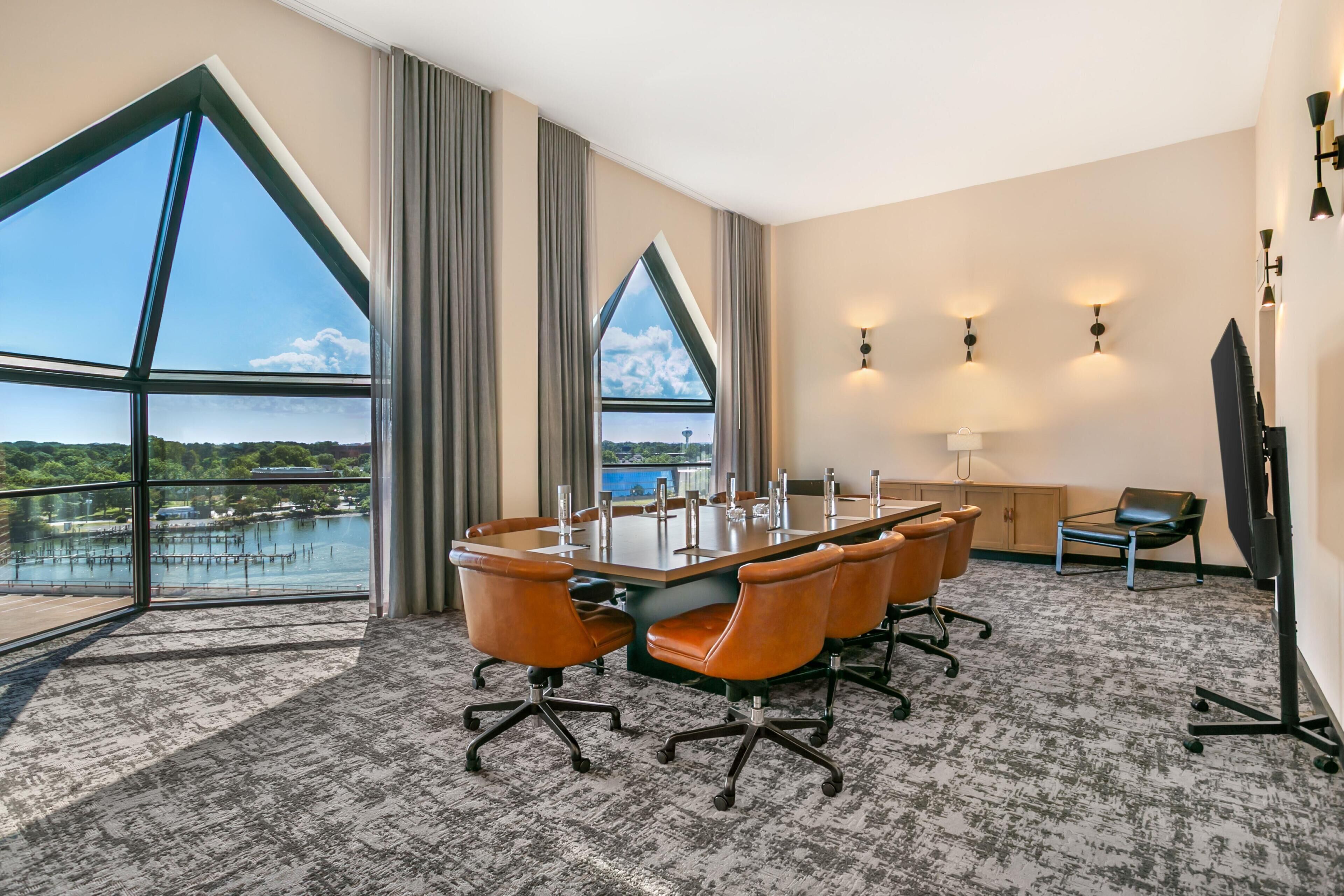 A conference room with a large table, chairs, and a view of a body of water through large windows.