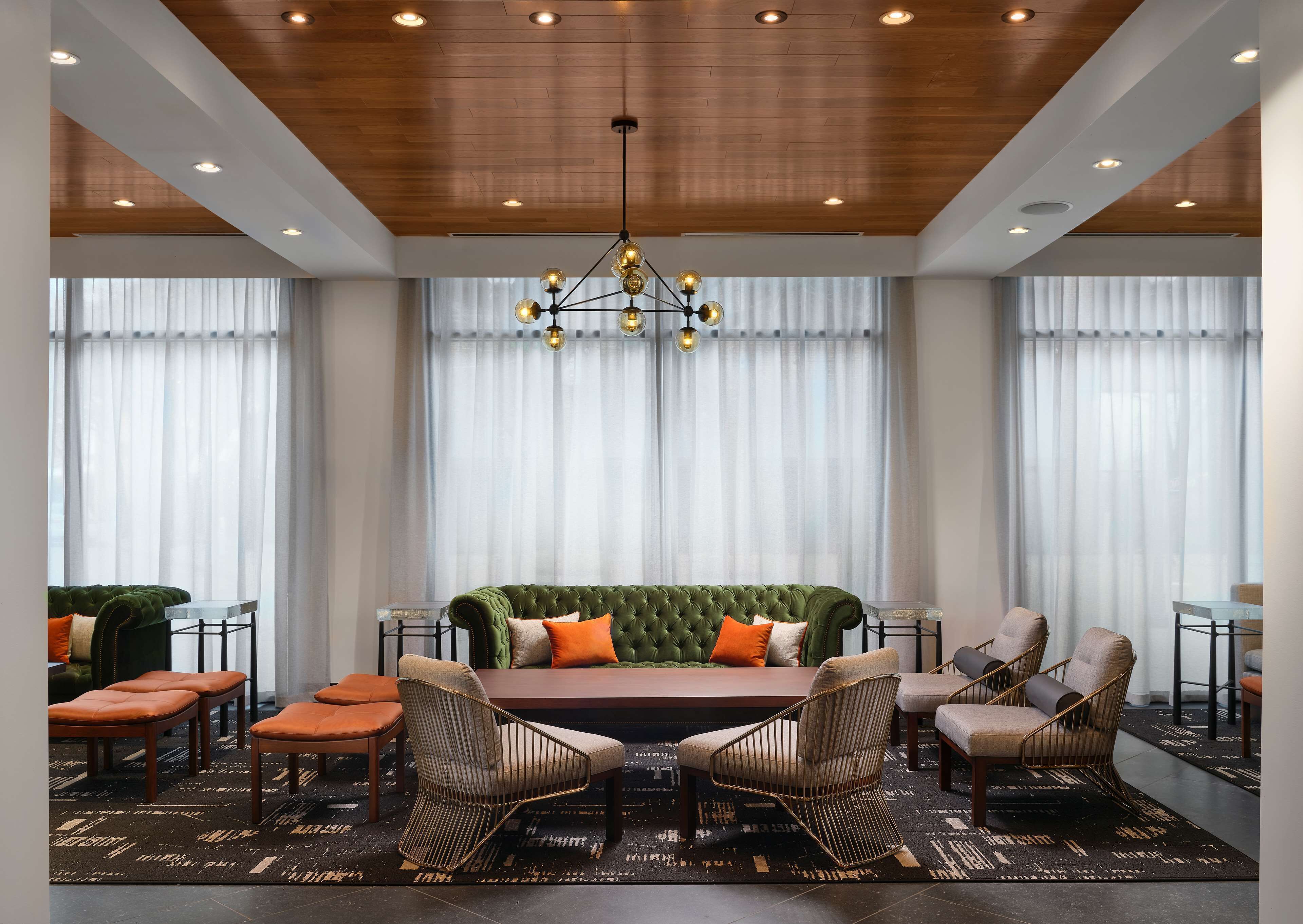A modern hotel room with a green sofa, two armchairs, a dining table, and a chandelier.