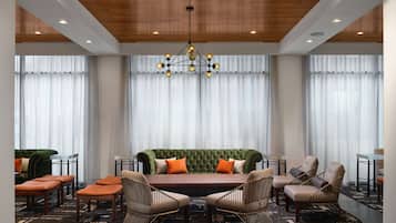 A modern hotel room with a green sofa, two armchairs, a dining table, and a chandelier.