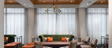 Una habitación de hotel moderna con un sofá verde, dos sillones, una mesa de comedor y una araña.